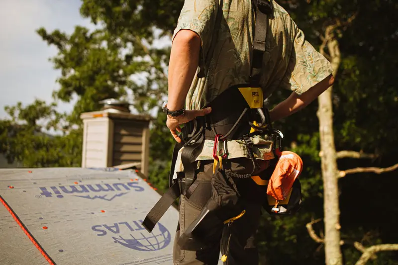 A roofer in a safety harness over new underlayment