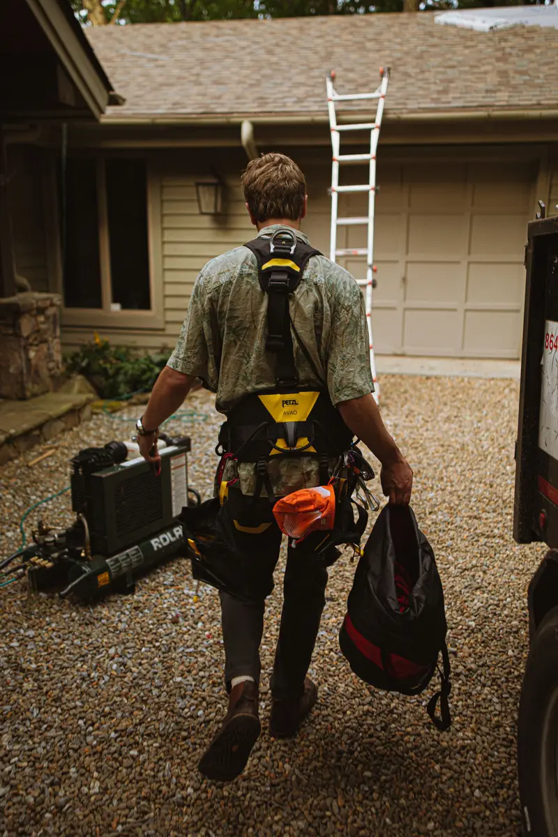 A roofer in a harness walking up a driveway with gear